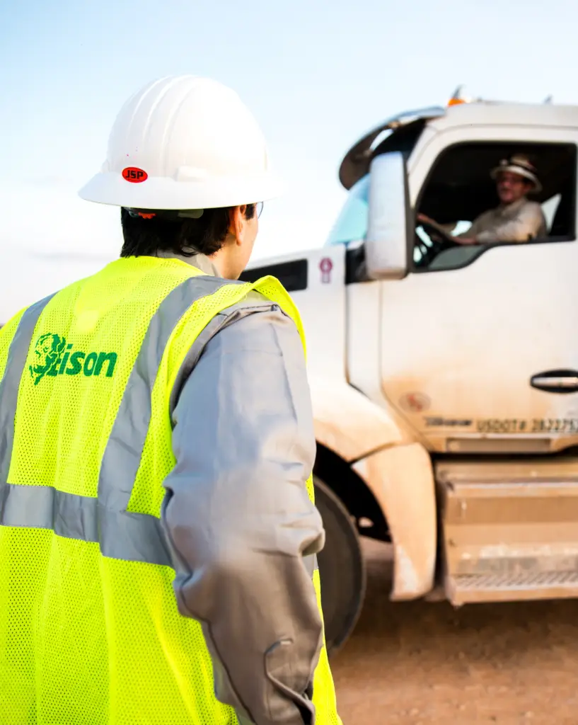 Bison team member in a high-visibility vest and hard hat communicating with a truck driver in the oilfield, symbolizing trust and service in the energy industry.