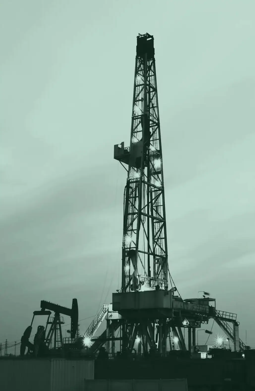 Illuminated oil drilling rig at dusk with pumpjack and workers in the foreground, representing the energy sector.